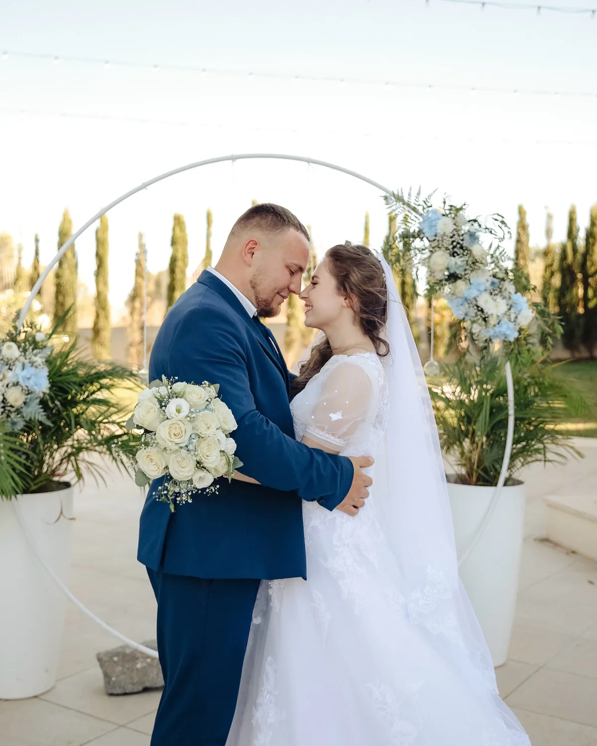 Noivos abraçados sob o arco floral branco